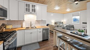 A modern kitchen with white cabinets, a wooden ceiling, and a dining area with a bench and table.