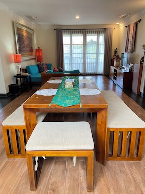 A spacious living room with a wooden dining table, cushioned benches, a sofa, and a television.