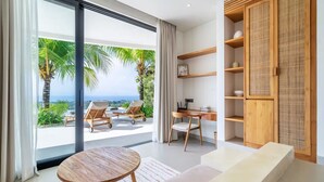 Ein modernes Wohnzimmer mit einem großen Schiebeglasfenster, das auf einen Balkon mit Blick auf Palmen und das Meer führt.