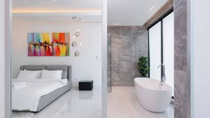 Un dormitorio moderno con una cama, un cuadro grande y un baño con bañera y una planta.