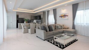 Una sala de estar moderna con un sofá modular, una mesa de centro de vidrio y un comedor al fondo.
