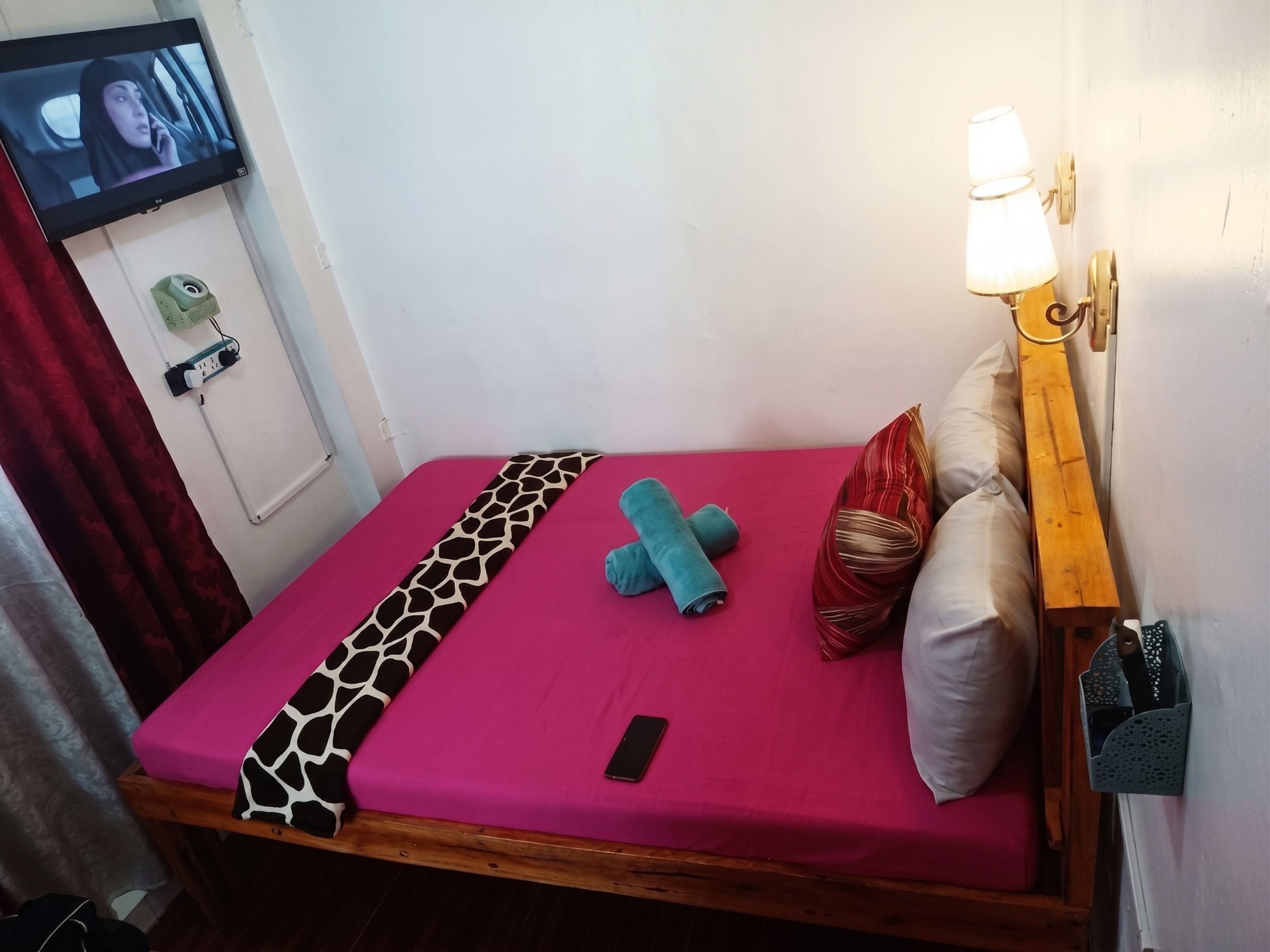 Un letto singolo con una coperta rosa acceso, una coperta fantasia e uno smartphone sul letto.