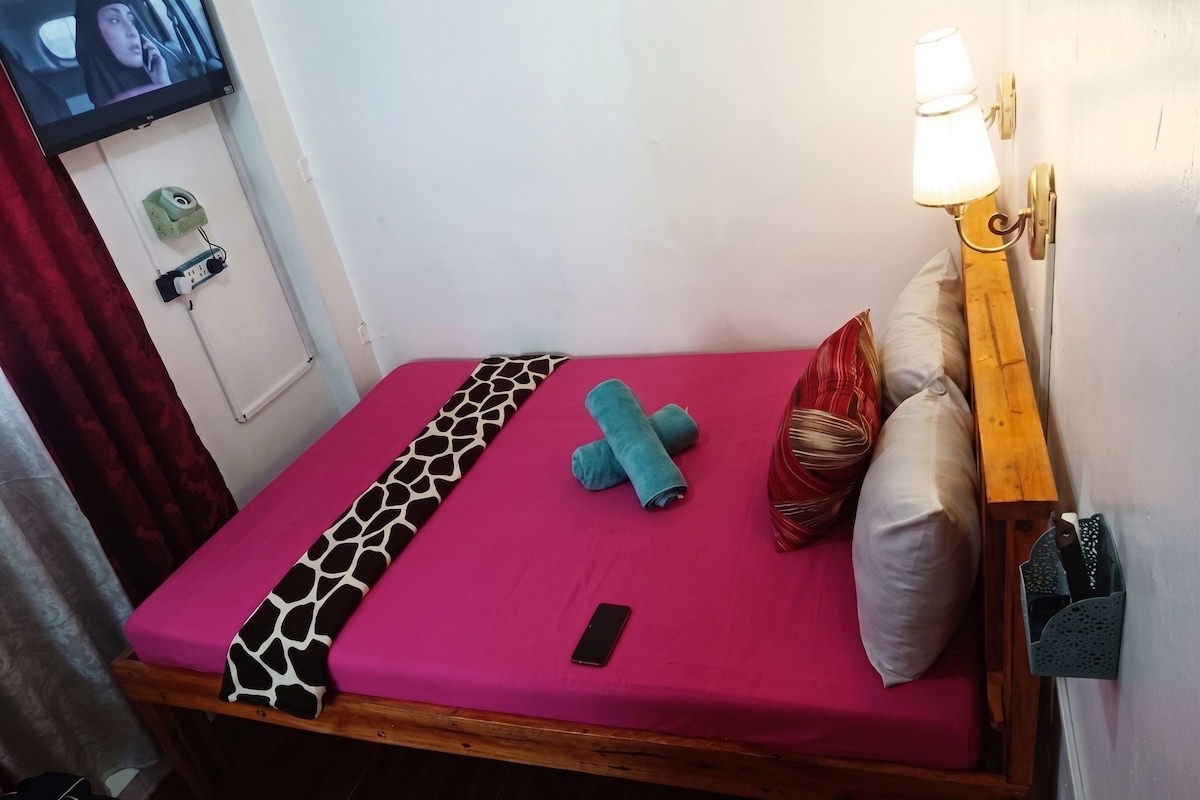 A single bed with a bright pink bedspread, a patterned blanket, and a smartphone on the bed.