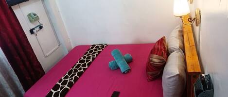 Un letto singolo con una coperta rosa acceso, una coperta fantasia e uno smartphone sul letto.