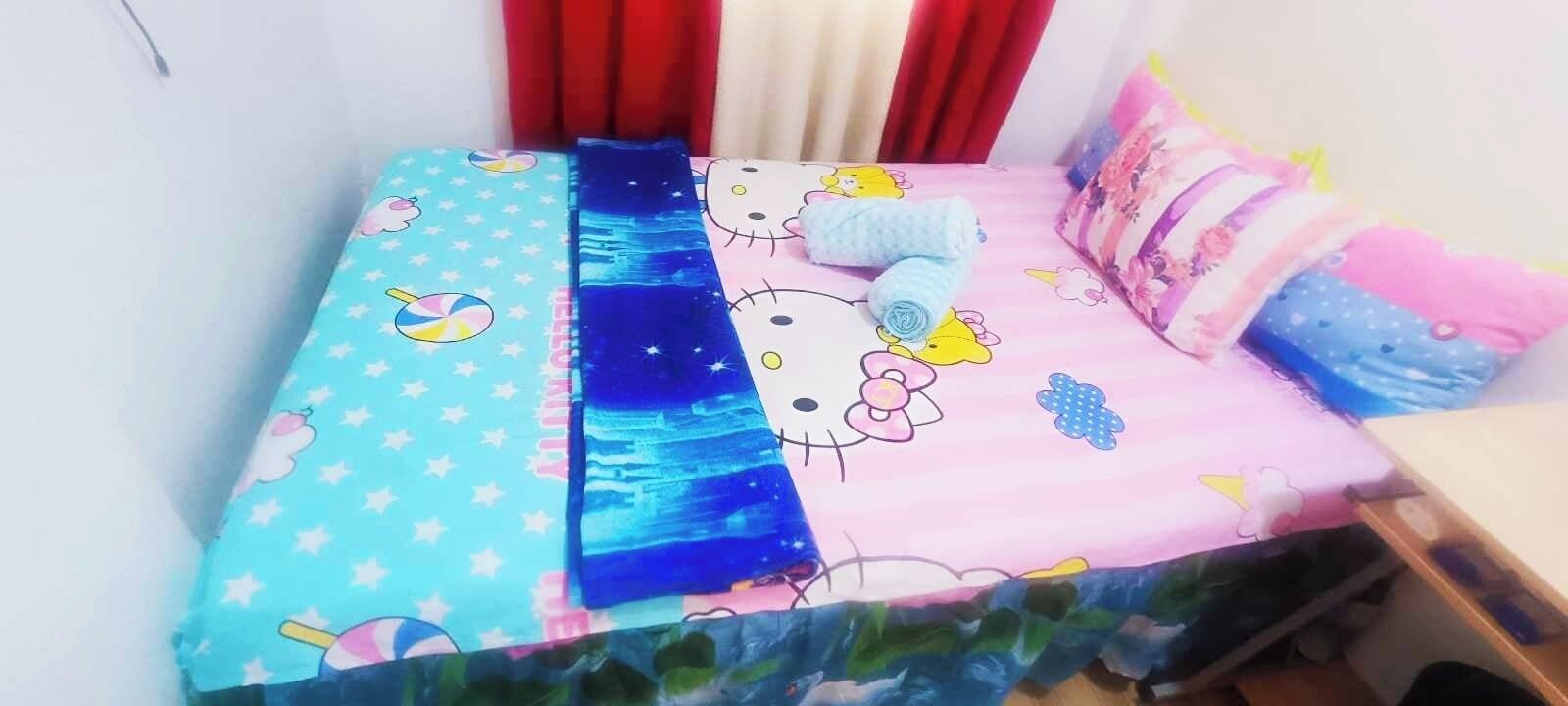 A bed with a Hello Kitty and Hello Moon design, a blue blanket, and pink pillows.