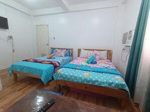 A room with two wooden beds, each with a colorful bedspread, a wooden table, and a door.