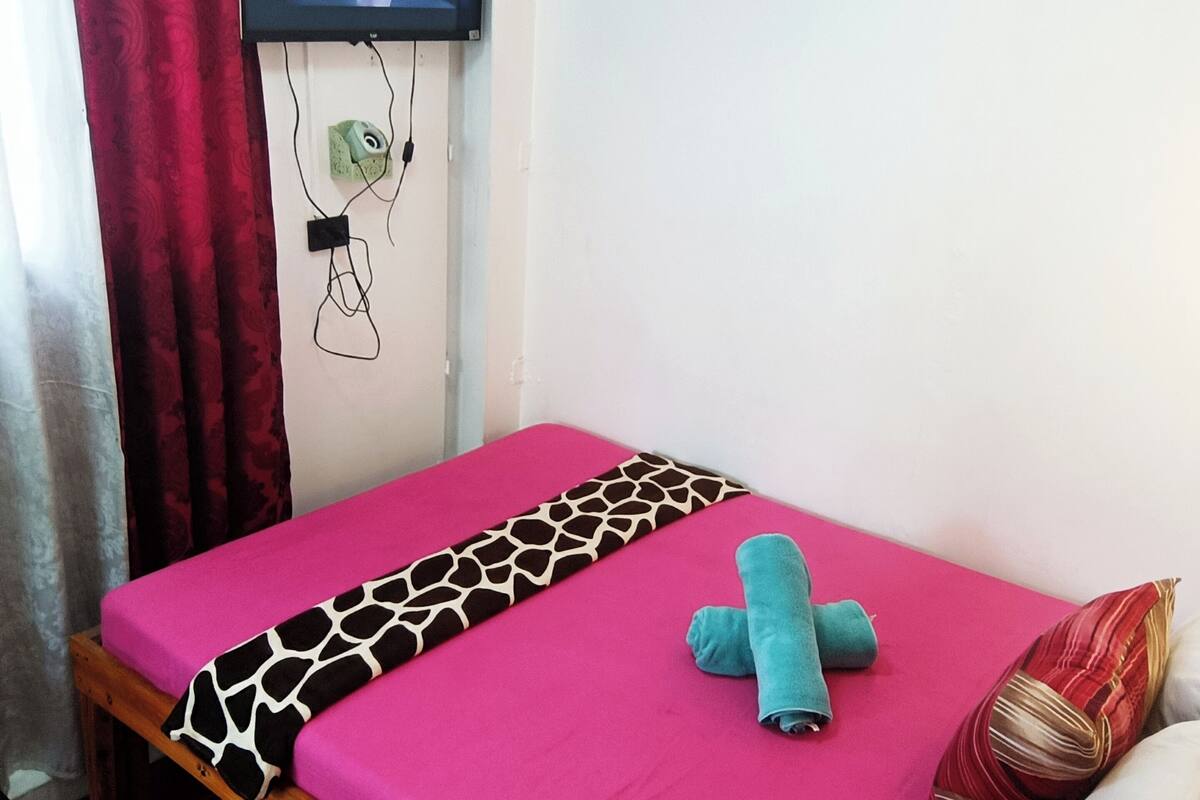 A single bed with a pink mattress, a black and white patterned blanket, a blue towel, and a smartphone on the bed.