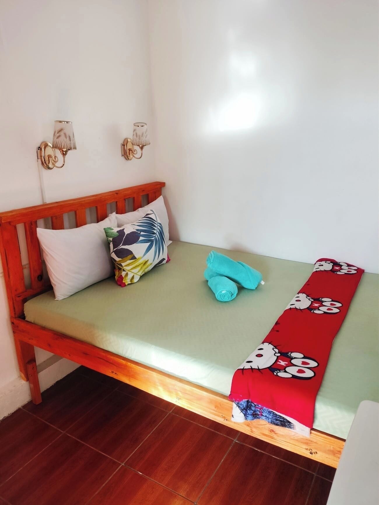 Una cama individual con cabecera de madera, colchón verde y manta roja con personajes de dibujos animados.