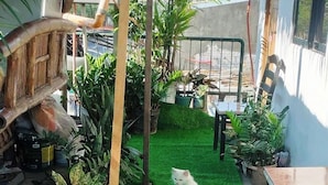 Un pequeño espacio al aire libre con césped artificial, rodeado de plantas en macetas y una estructura de madera.