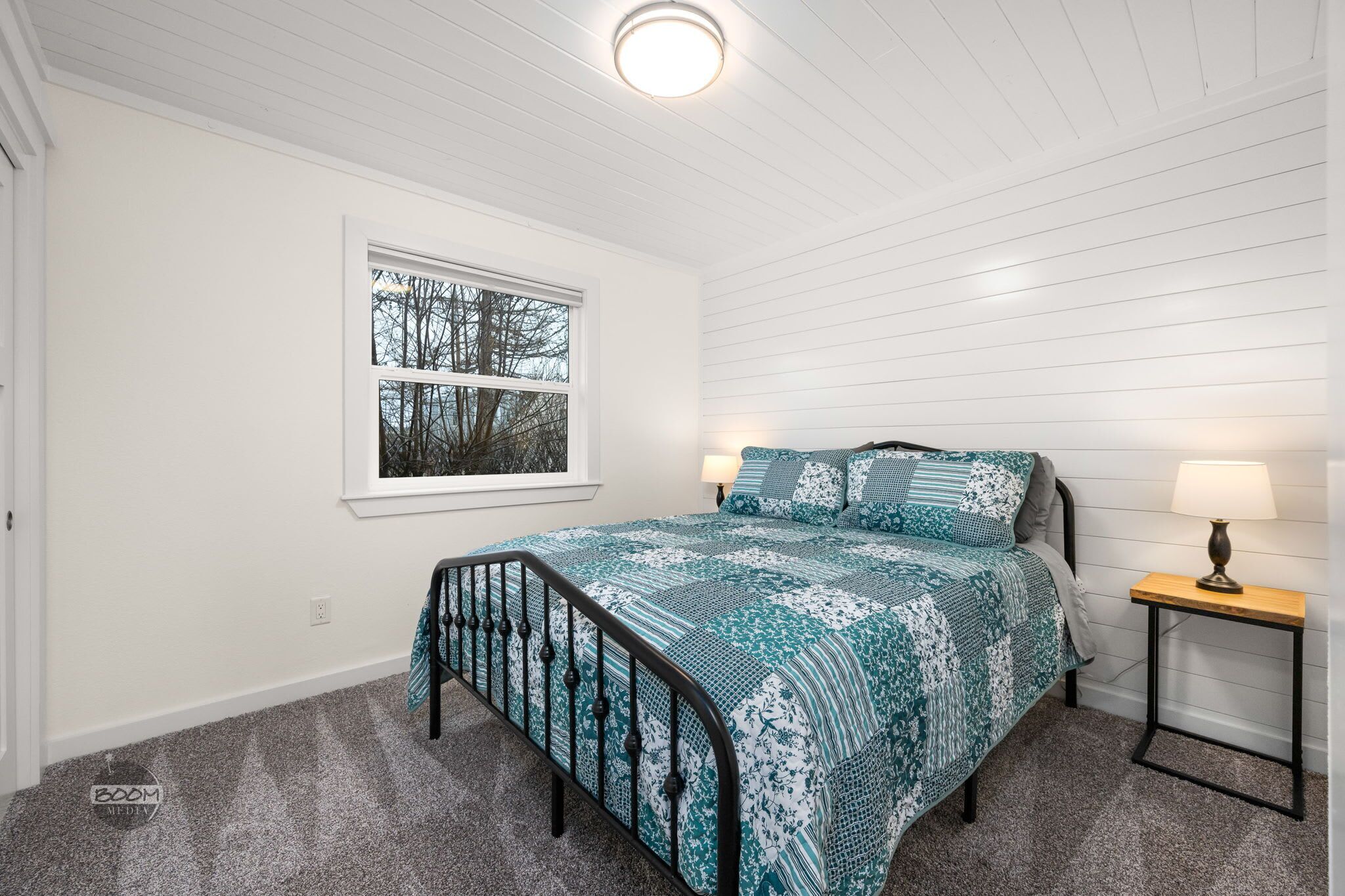 Ett sovrum med en säng, två sänglampor, ett fönster med utsikt och en taklampa.