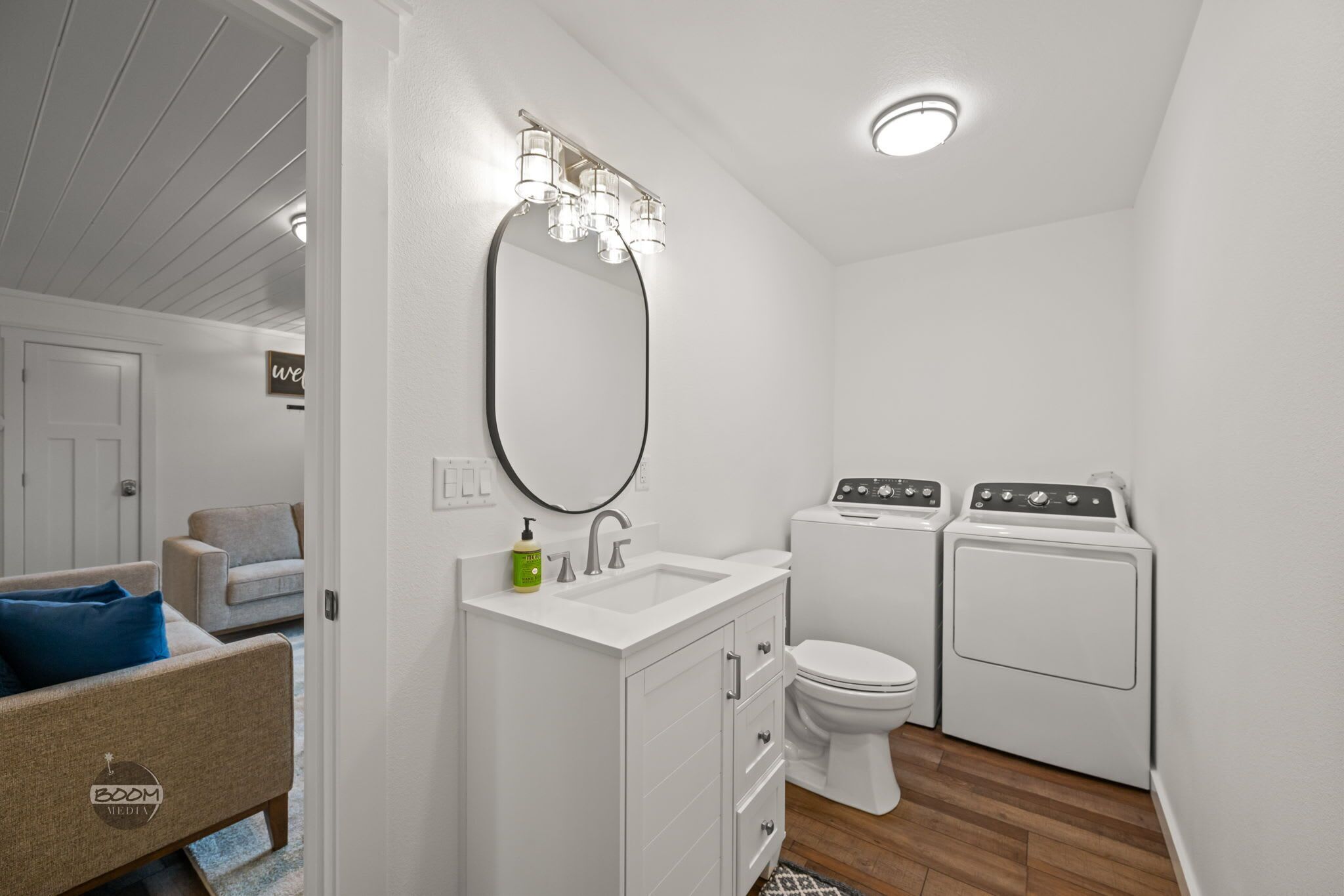 Casa de banho compacta com lavatório branco, espelho, sanita e duas máquinas de lavar roupa empilhadas.