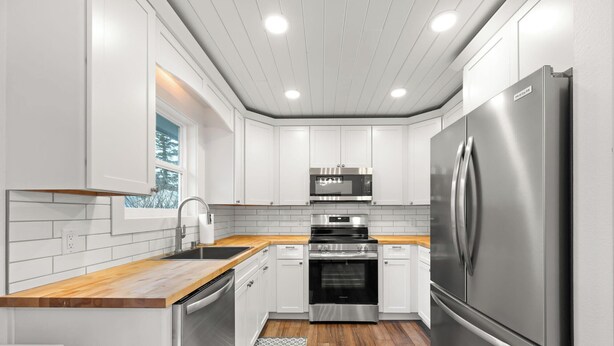 A modern kitchen with white cabinetry, stainless steel appliances, and a wooden countertop. - Adorable Downtown Cottage - Walk to Shops & Cafes! (Palmer)