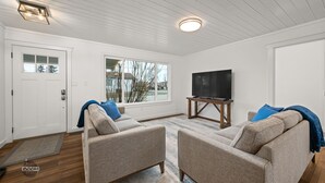 A living room with two sofas, a television on a stand, and a door with a window. - Adorable Downtown Cottage - Walk to Shops & Cafes! (Palmer)