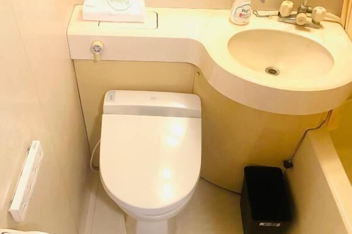 A bathroom with a toilet, sink, and a trash bin.
