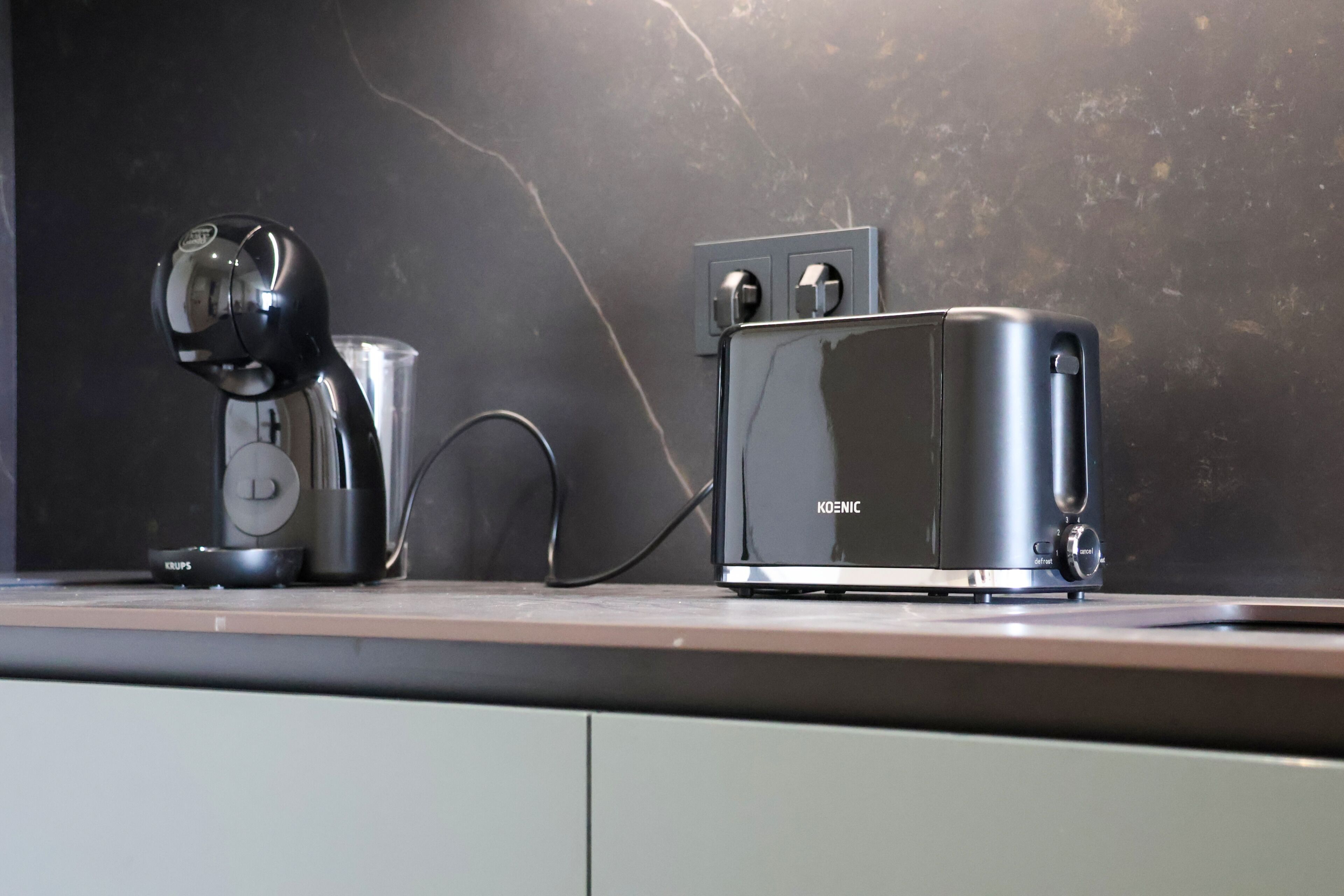 Una cocina con cafetera, tostadora y un vaso de agua sobre la encimera.