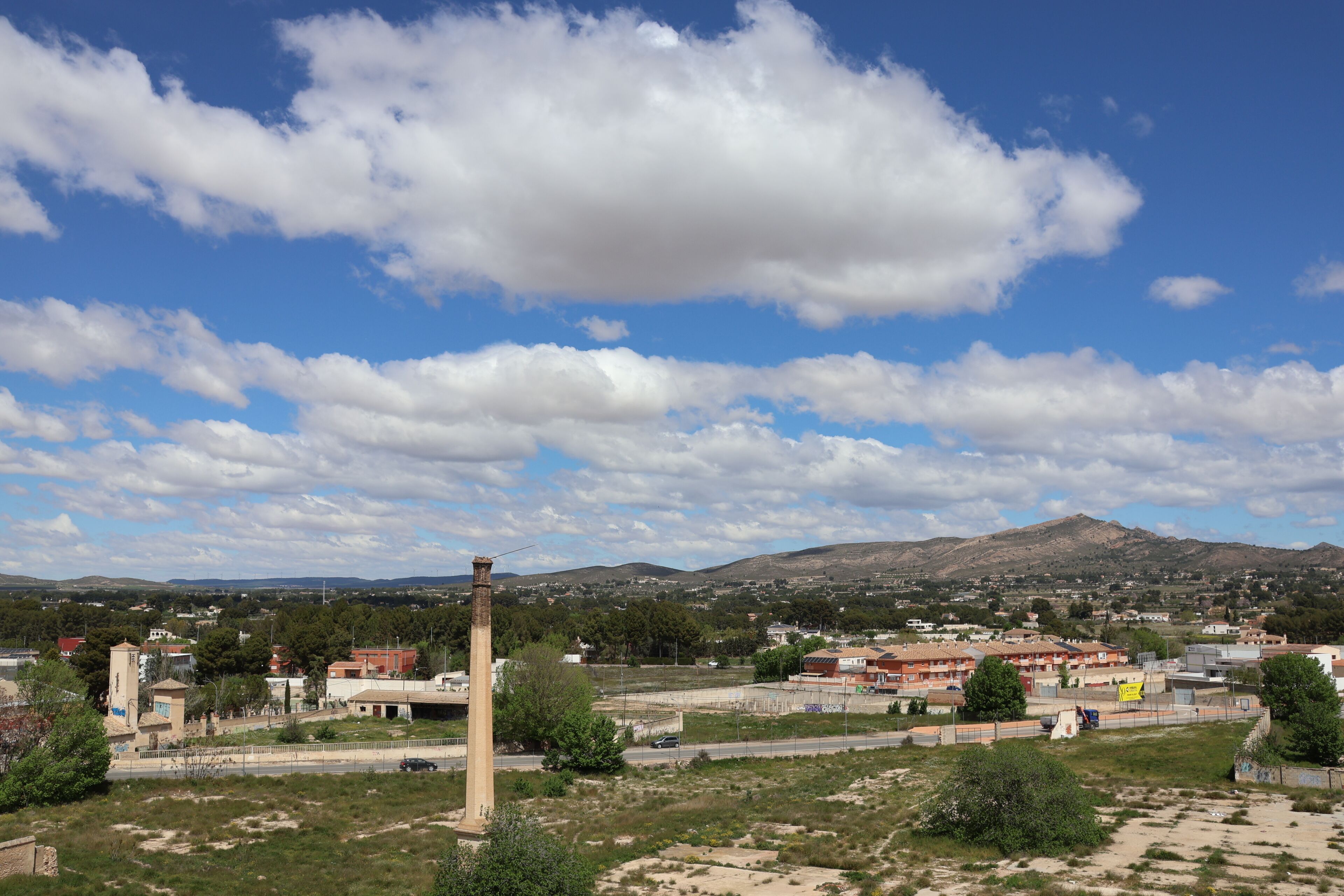 Un paisaje con una torre destacada, una carretera y edificios a lo lejos.