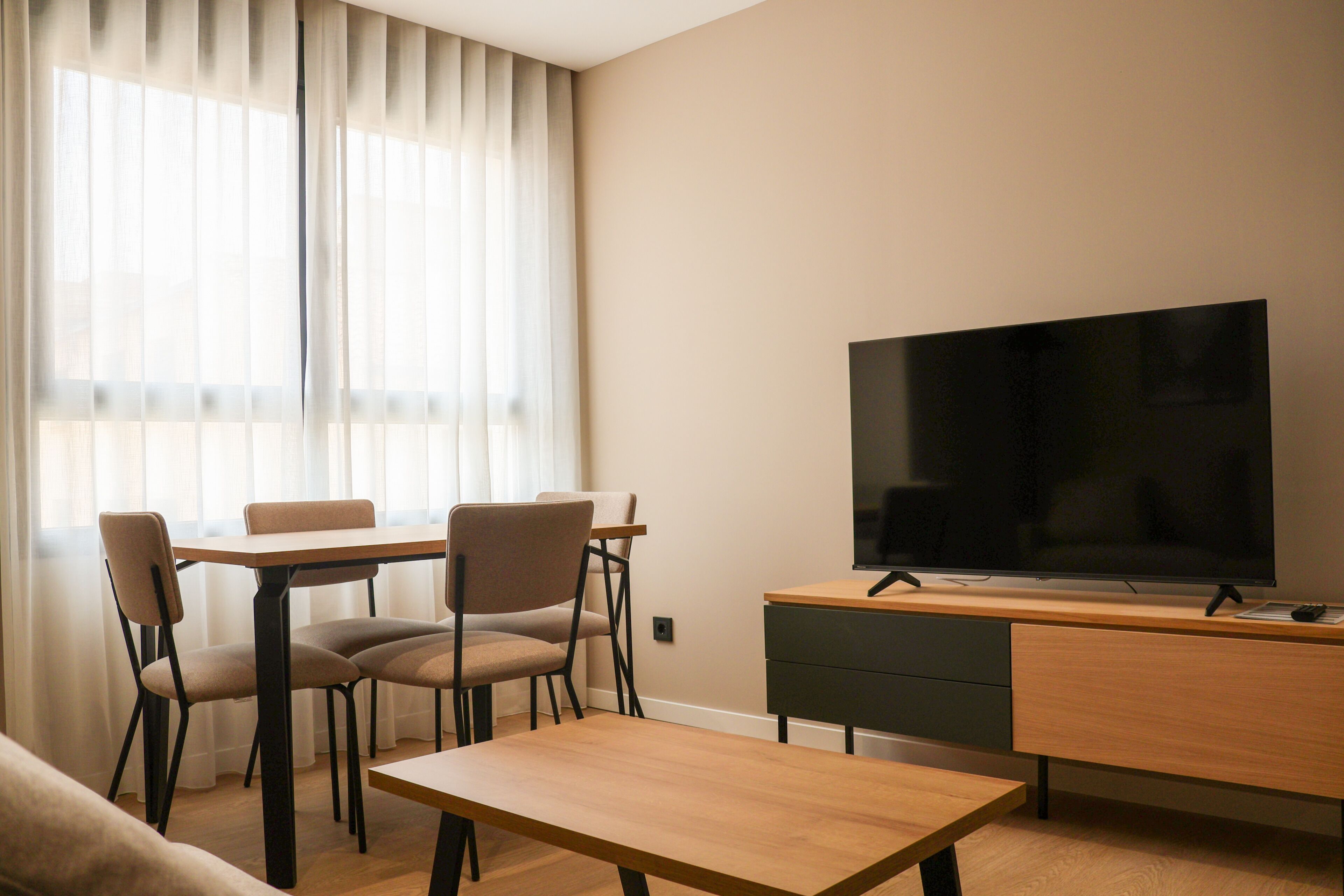 Una sala moderna con una televisión de pantalla plana, una mesa de centro de madera, dos sillones, un sofá y una mesa de comedor.