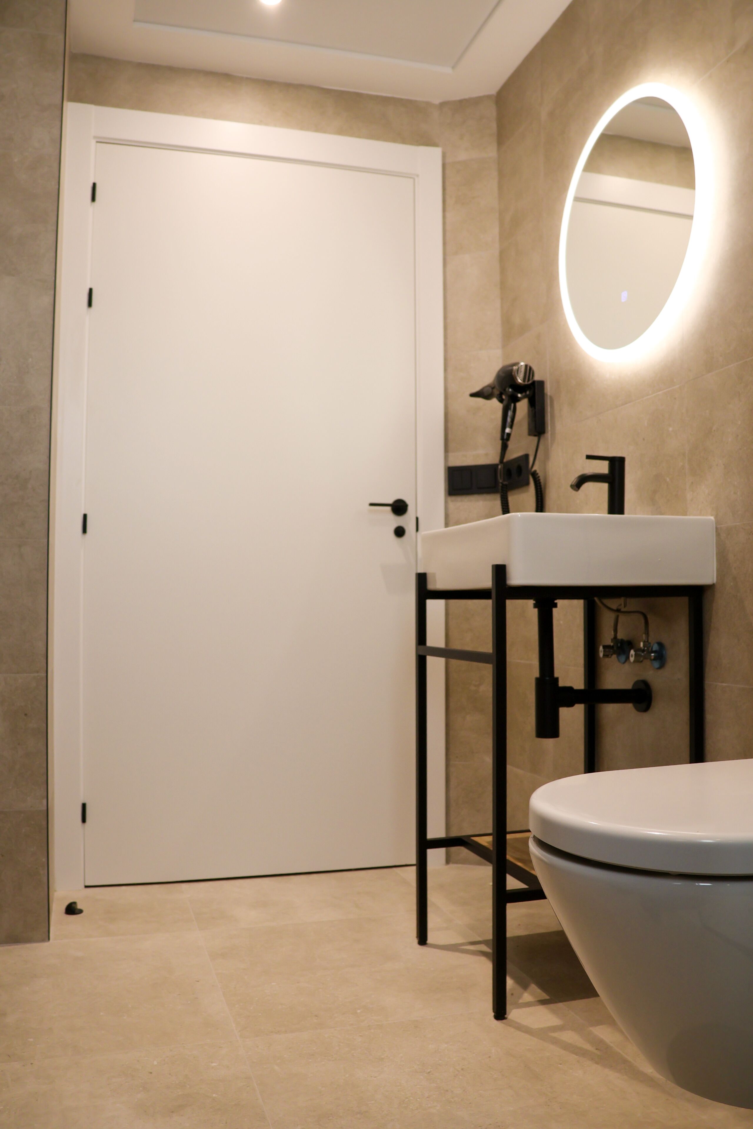 Un bagno moderno con un WC bianco, un lavabo con struttura nera e uno specchio illuminato.