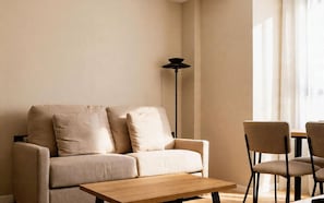Een woonkamer met een bank, twee stoelen, een salontafel, een vloerlamp en een raam met gordijnen.