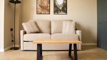 Una sala de estar con un sofá color beige, una mesa de centro de madera y dos cuadros en la pared.