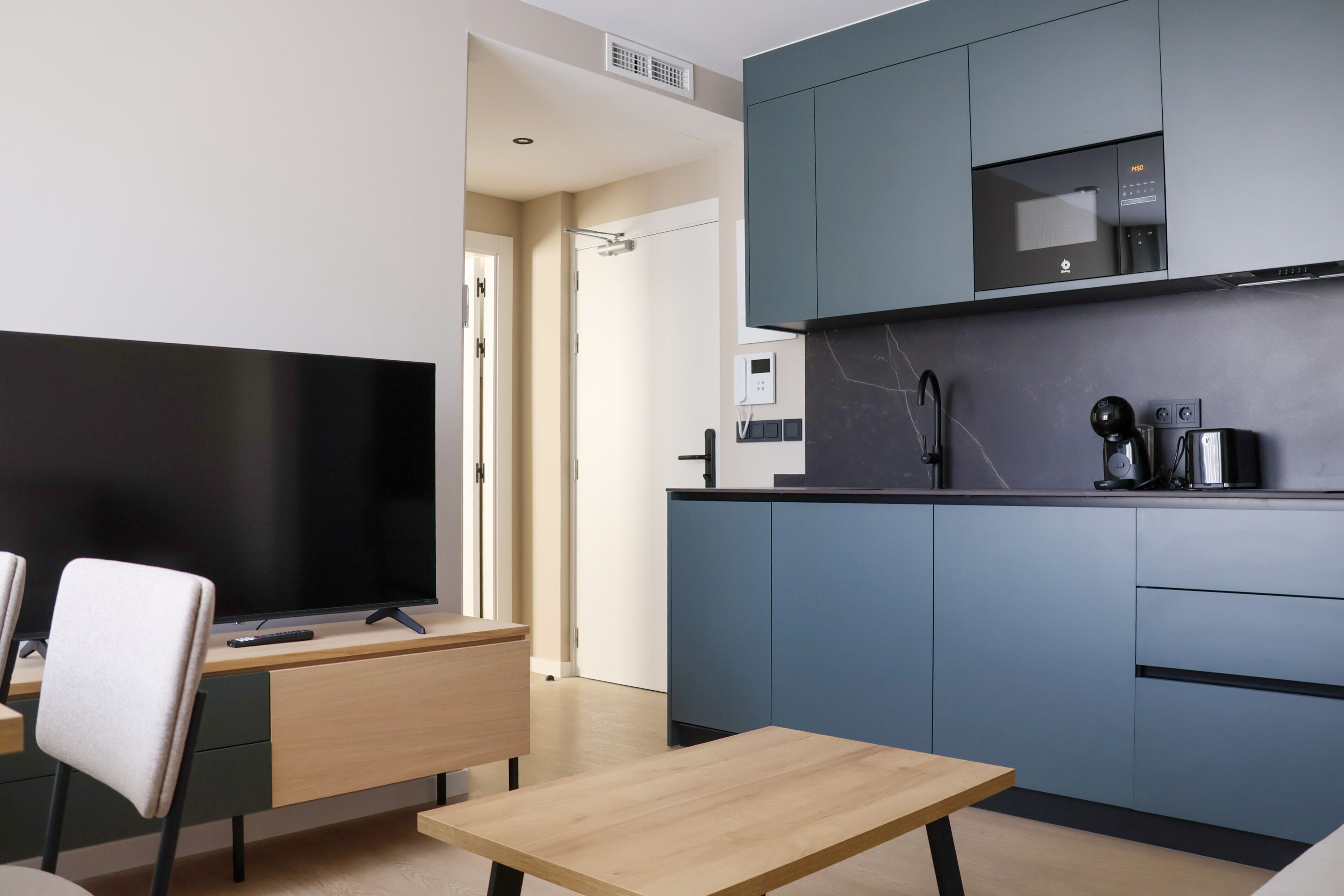 A modern kitchen with a flat-screen TV, a coffee machine, and a microwave.