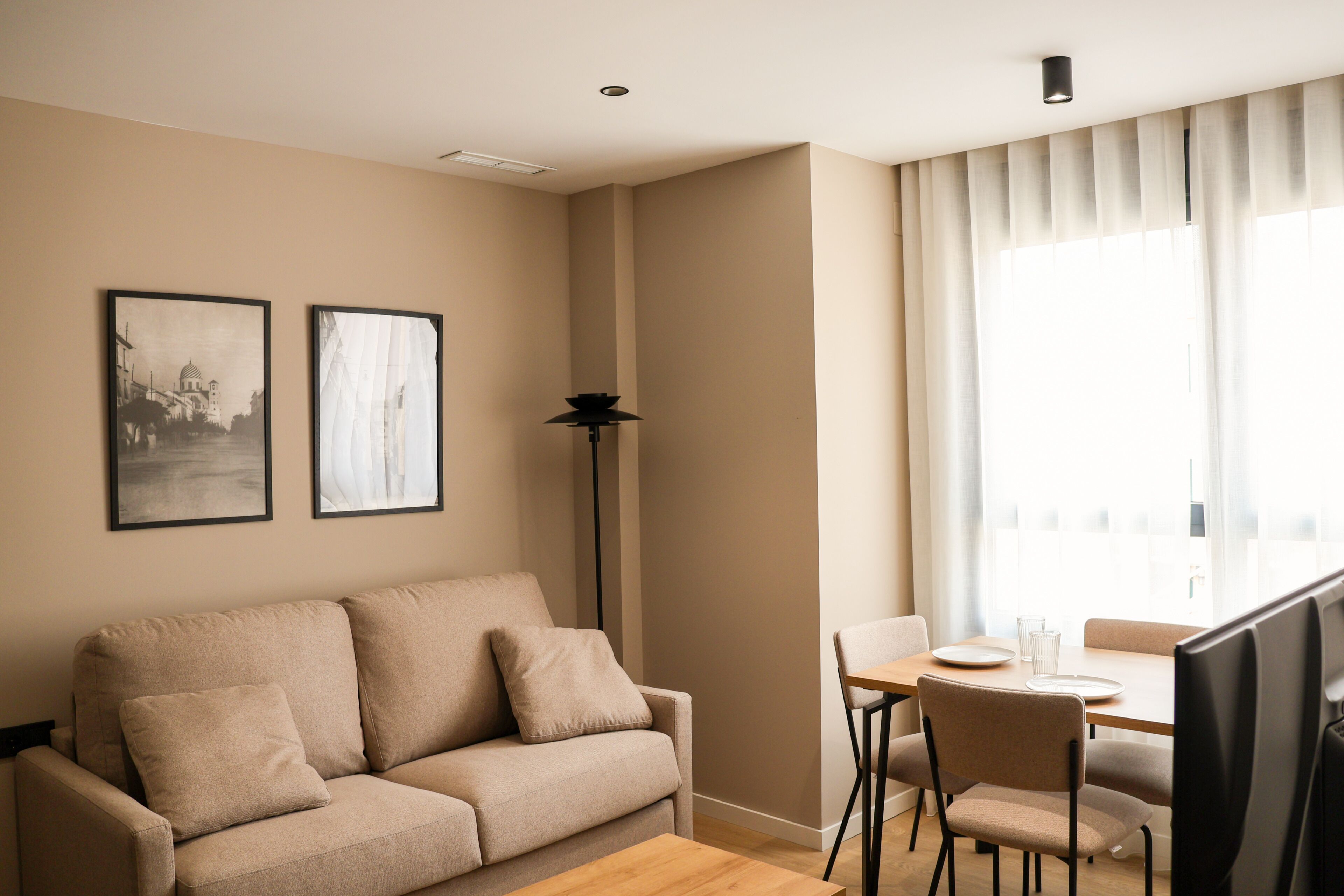 Una sala de estar moderna con un sofá, una mesa de comedor, sillas y dos cuadros en la pared.