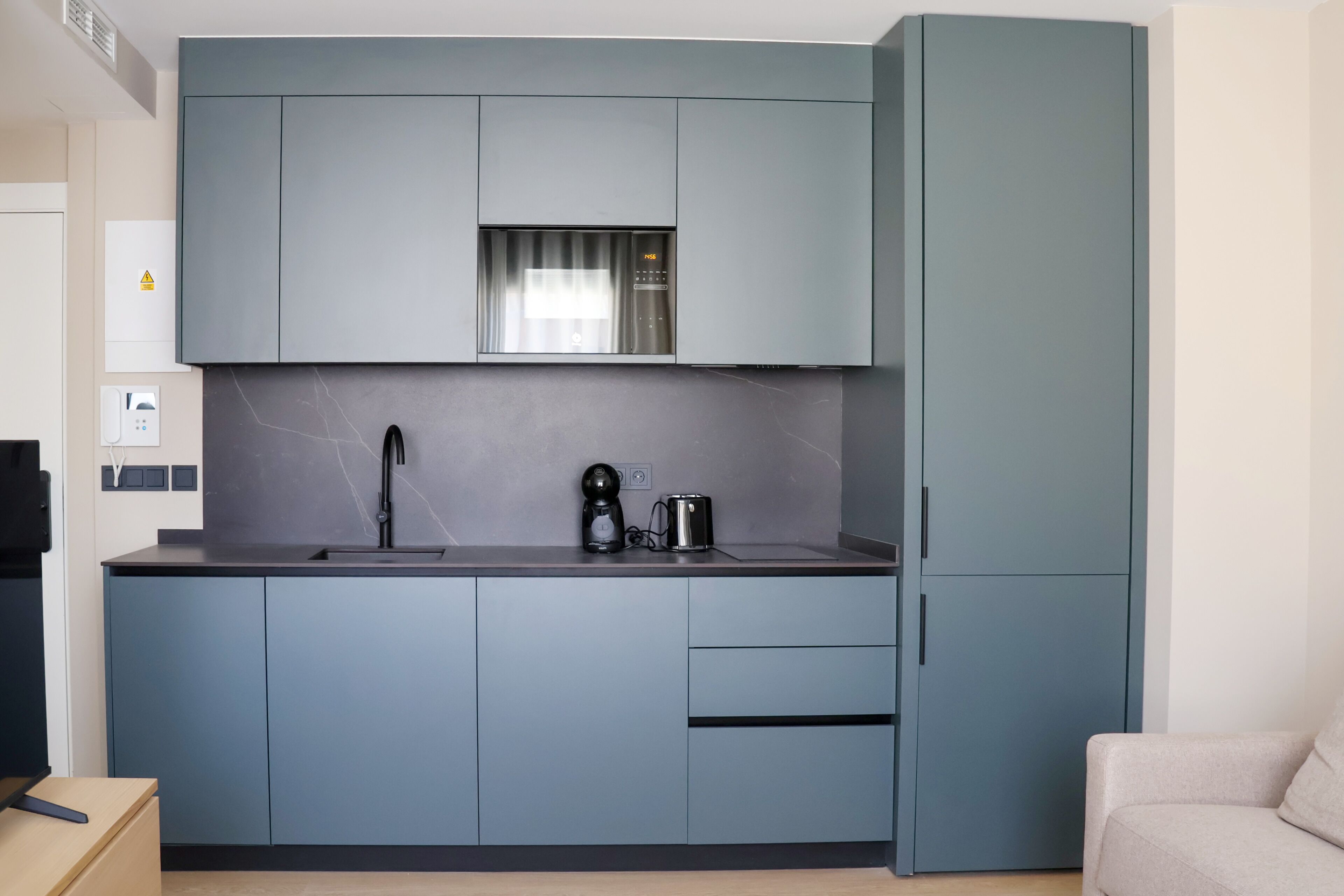 A modern kitchen with grey cabinets, a stainless steel range hood, a coffee maker, and a toaster.