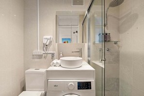 A modern bathroom with a built-in washing machine, a sink, and a glass-enclosed shower. - The Postcard - Harbour Bridge & Opera House Views (North Sydney)