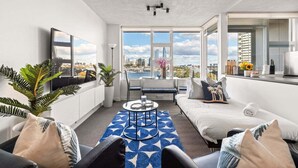 Un salon moderne avec un canapé, une table basse et une vue sur le paysage urbain, visible à travers de grandes fenêtres.
