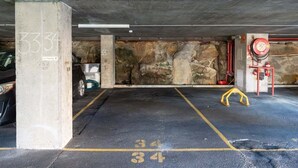 Un parking souterrain avec des piliers en béton, des places de stationnement numérotées et un enrouleur de tuyau d’incendie.