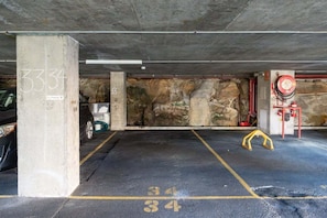 A parking garage with concrete pillars, numbered parking spaces, and a fire hose reel. - The Postcard - Harbour Bridge & Opera House Views (North Sydney)