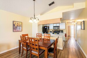 A dining area with a wooden table and chairs, a kitchen in the background, and a hallway leading to other rooms. - ‼️Kissimmee Condo - Sleeps 8, Private Balcony (Kissimmee)