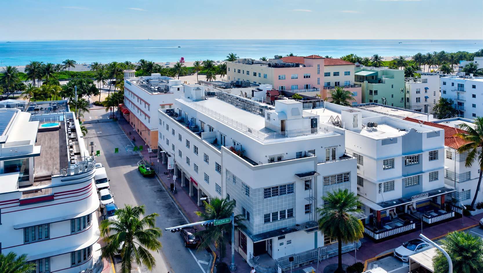 A multi-story hotel with a flat roof, a street view, and a beach in the background.