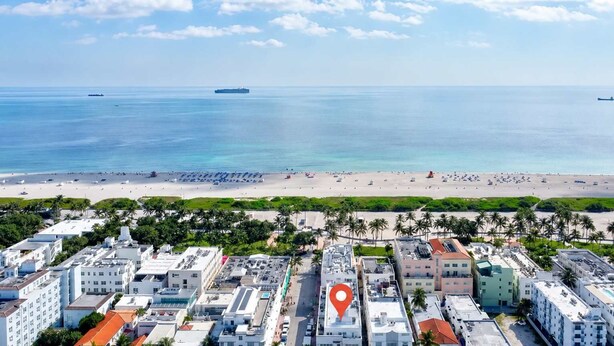 Luchtbeeld van een kuststad met een strand, gebouwen en een rode markering voor een locatie.