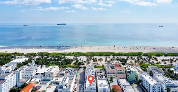 Ein Luftbild einer Küstenstadt mit Strand, Gebäuden und einem roten Markierungszeichen.
