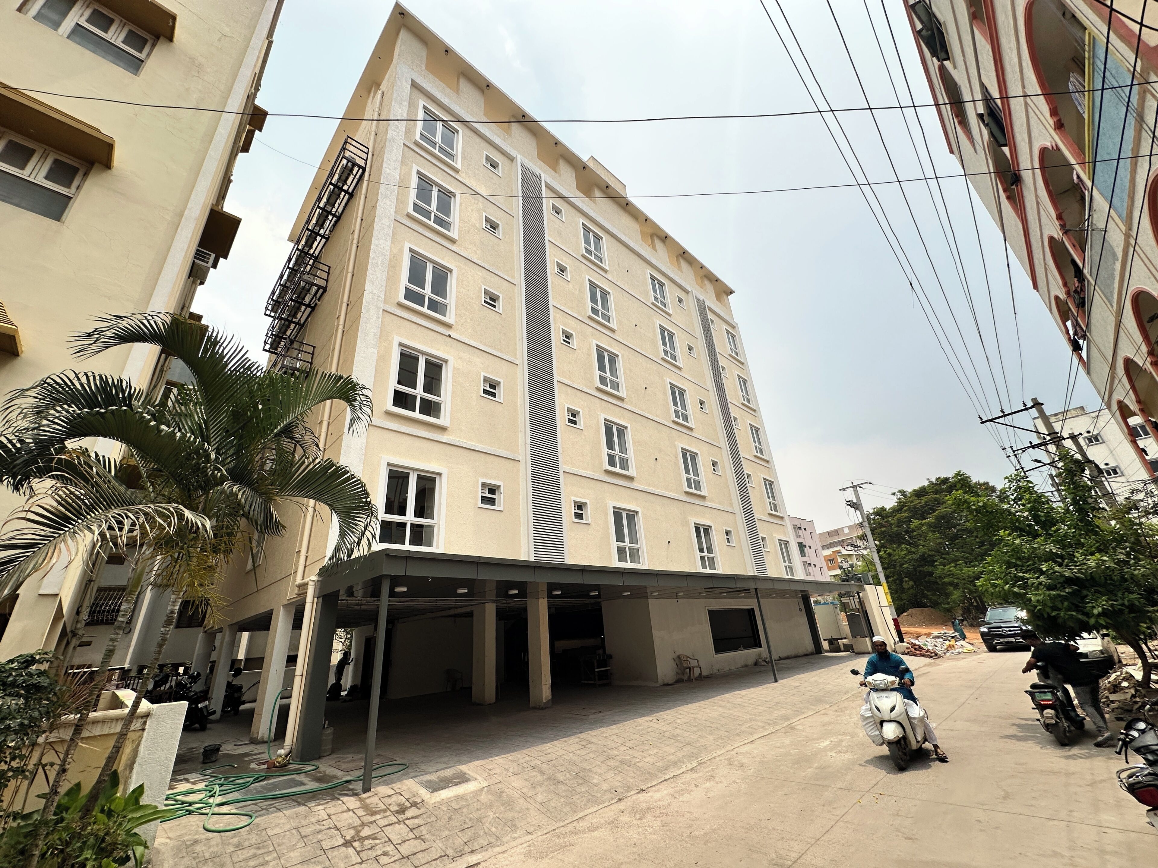 A multi-story building with a covered parking area, a staircase, and a palm tree.