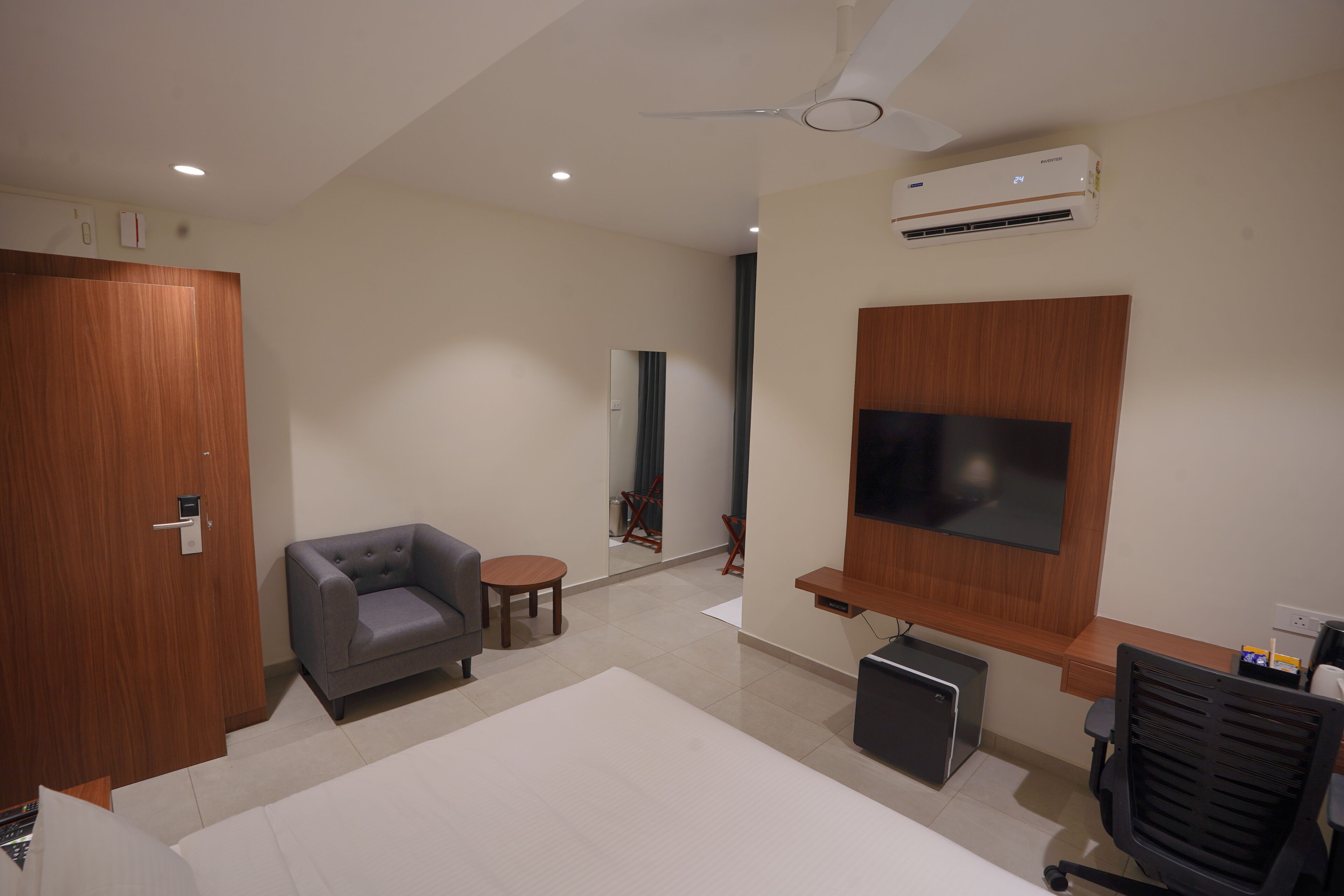 Une chambre d’hôtel moderne équipée d’un téléviseur à écran plat, d’un bureau, d’une chaise, d’un canapé, d’une petite table et d’une armoire.