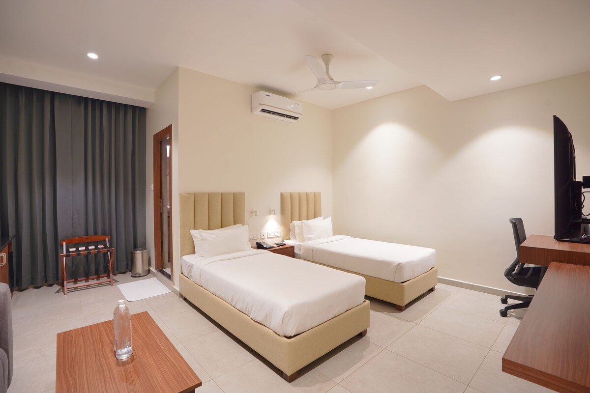 Habitación de hotel con dos camas, un escritorio, una silla, lámpara de escritorio, unidad de aire acondicionado y ventilador de techo.