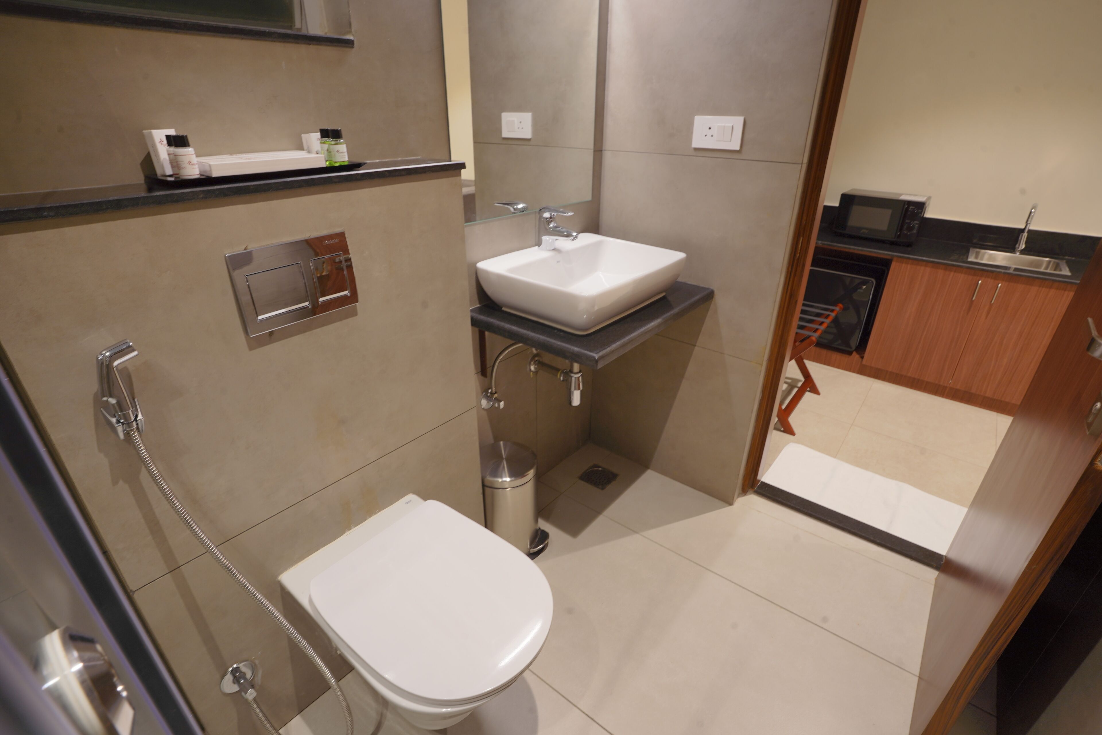 A compact bathroom with a toilet, sink, shower, and a microwave in the adjacent kitchen area.