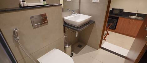 A compact bathroom with a toilet, sink, shower, and a microwave in the adjacent kitchen area.