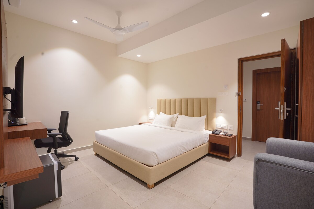 Un dormitorio con cama, escritorio, silla, mesitas de noche y una puerta.