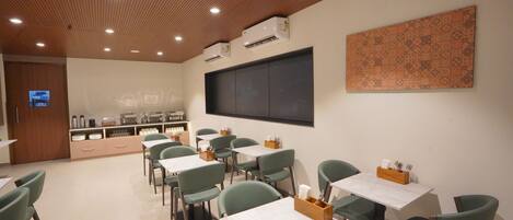 A dining area with green chairs and white tables, a wooden ceiling, and a large patterned wall.