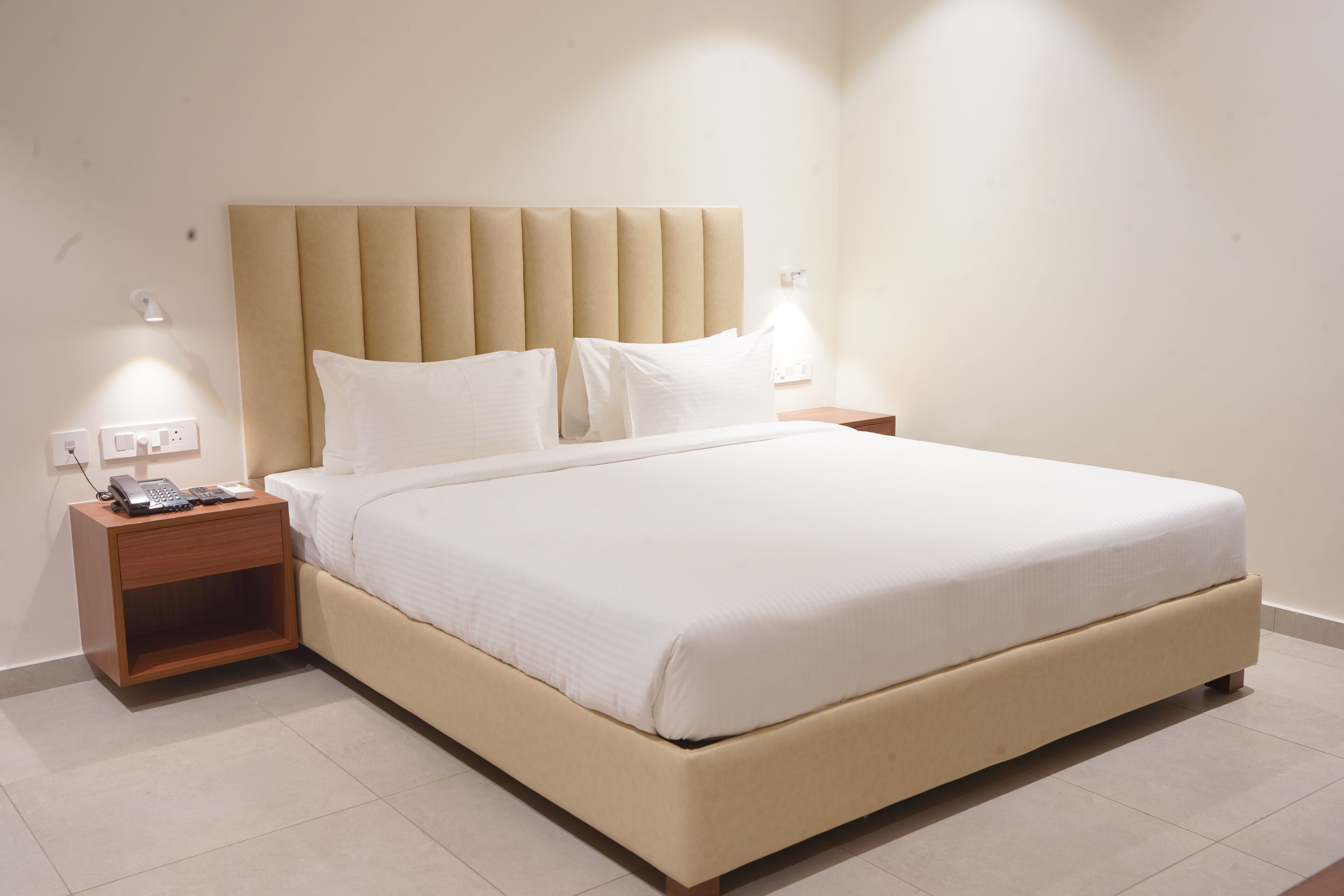 Cama bem arrumada com cabeceira acolchoada, mesa de cabeceira com abajur e tomada.