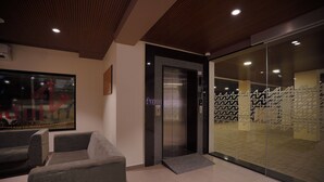A modern lobby with a reception desk, a glass elevator, and a patterned wall. - Hotel Jubilee Park Hitech city (Hyderabad)