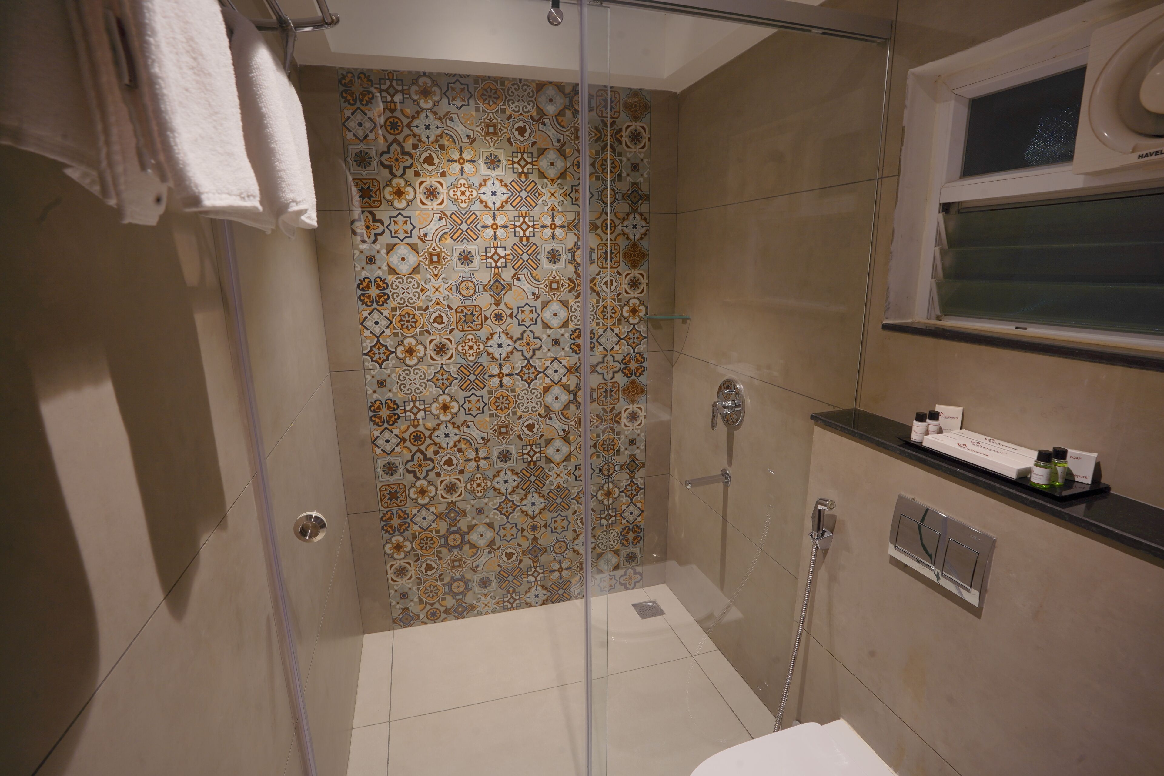 A shower with a glass door, a tiled wall, and a window above the sink.