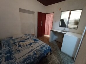 A bedroom with a bed, a small desk with a sink, a mirror, and a red door. - Yellow House (Antigua Guatemala)