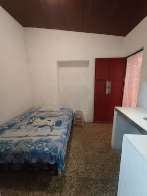 A small room with a bed, a stool, a red door, and a white counter. - Yellow House (Antigua Guatemala)