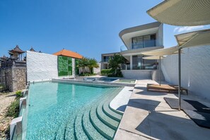 A modern pool area with clear water, a stone wall, and a traditional building in the background. - LegKo Villa (Pecatu)