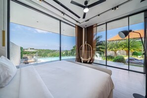 A modern bedroom with a large bed, a ceiling fan, and a view of a swimming pool and greenery. - LegKo Villa (Pecatu)