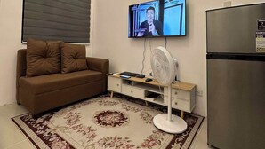 Een moderne woonkamer met een bank, televisie, ventilator en koelkast.